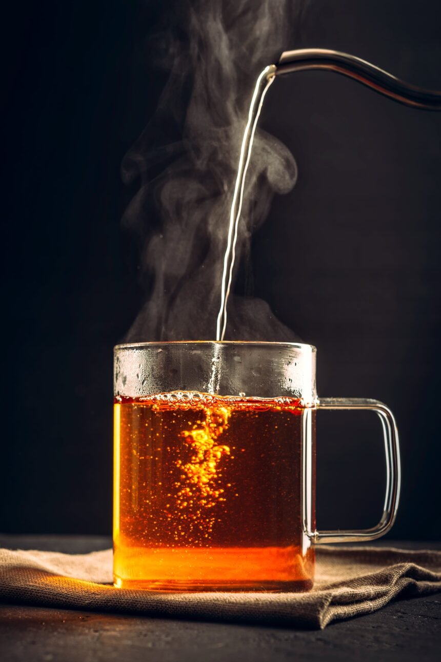 The process of brewing tea, pouring hot water from the kettle into the Cup, steam coming out of the mug, water droplets on the glass, black background