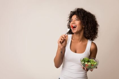 Web - comer melhor Excited african-american lady eating healthy salad over light background